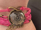 Armband - Dodecagram als nachtschwarzer ca. 25 mm großer Coin (hinter Glas) mit Goldlegierung in pinkes mehrsträngiges Band eingearbeitet
